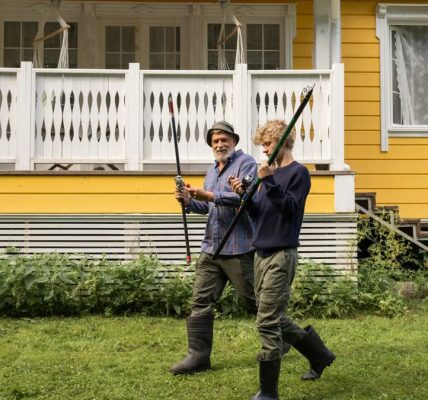 Elderly man and young boy with fishing rods in front of a yellow house, spending quality time outdoors.