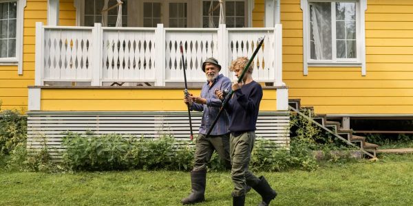 Elderly man and young boy with fishing rods in front of a yellow house, spending quality time outdoors.