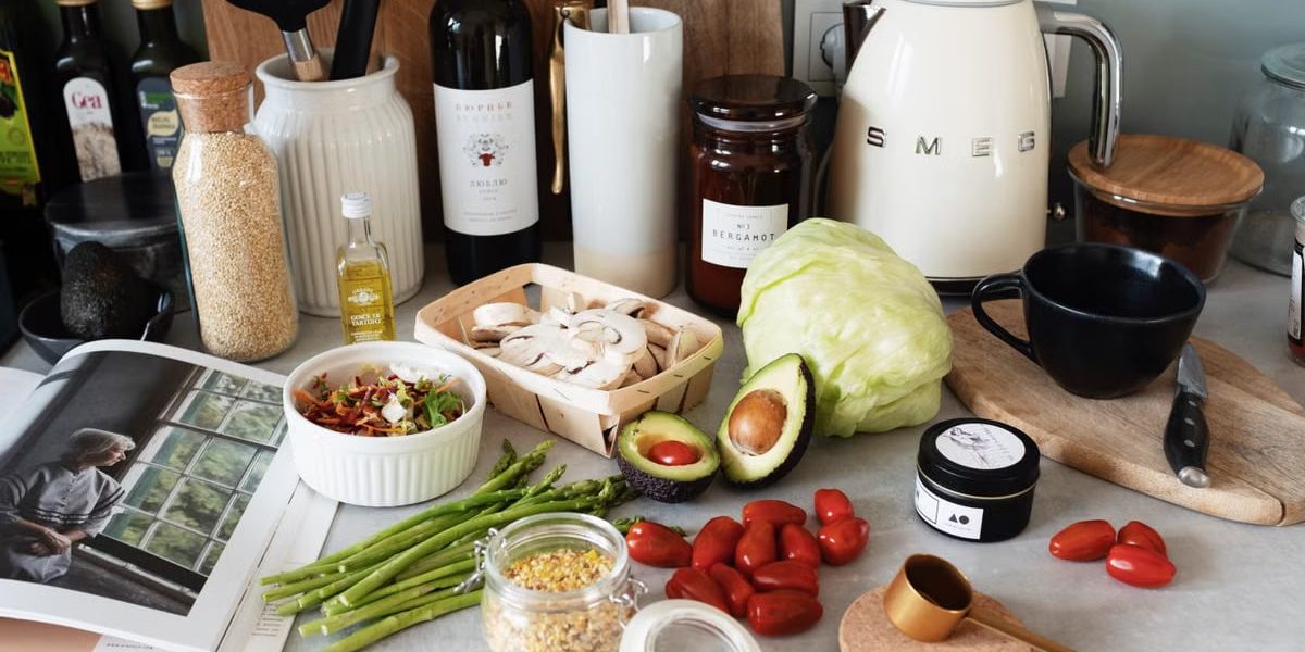 Assorted healthy food and vegetables set locating on gray countertop next to various utensils and appliances during cooking in stylish kitchen